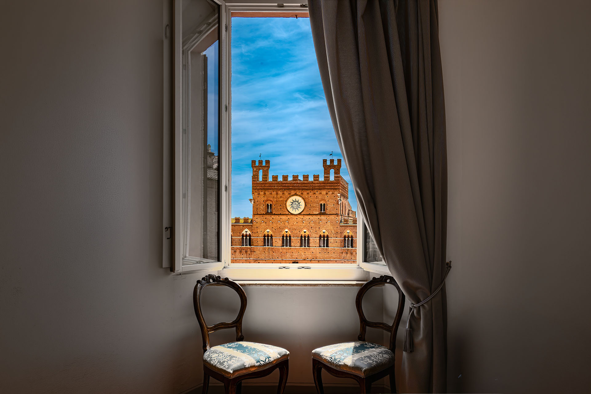 La veduta sul Palazzo Pubblico di Piazza del Campo da una finestra privata di palazzo, con due sedie d'epoca